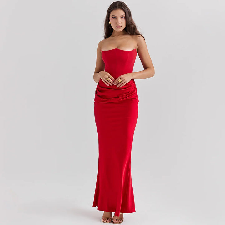 Woman wearing a strapless red evening gown with ruched waist and gold jewelry on gray background