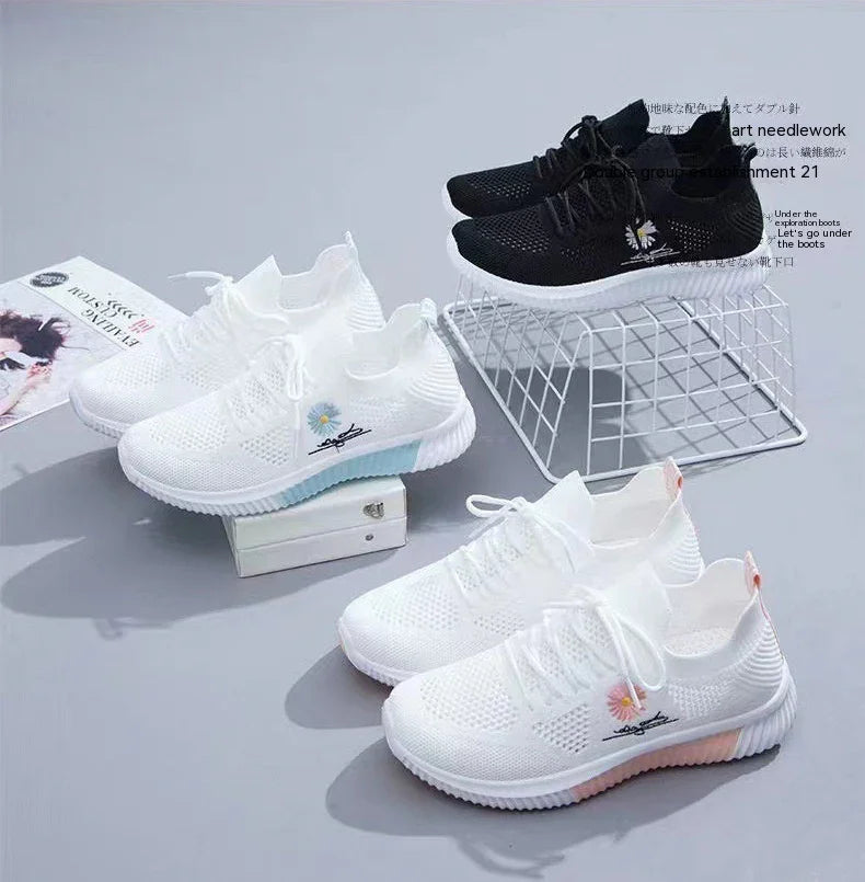 Three pairs of sporty knitted sneakers with floral embroidery in black, white with blue sole, and white with pink sole on gray surface