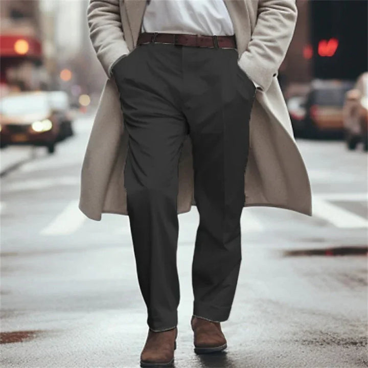 Man walking on city street wearing beige coat, black pants, white shirt, and brown boots