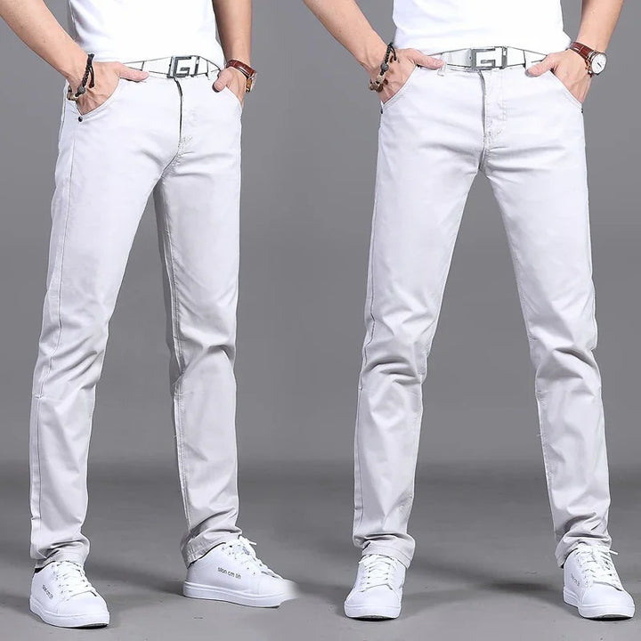 Men wearing slim fit light gray jeans, white sneakers, black bracelet, and brown wristwatch on gray background