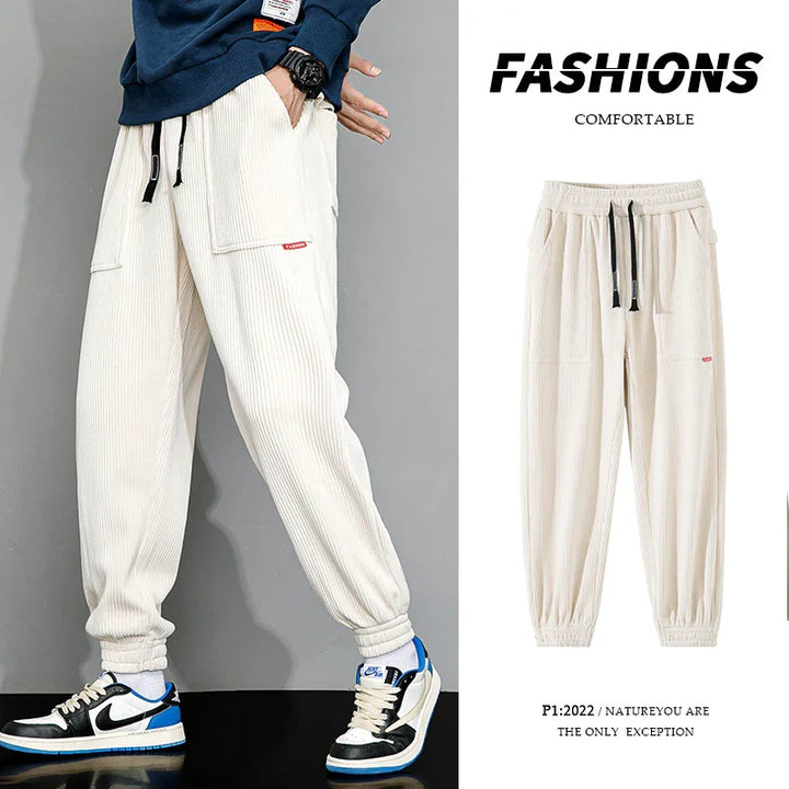 Beige casual corduroy jogger pants with elastic cuffs and black drawstrings, styled with sneakers