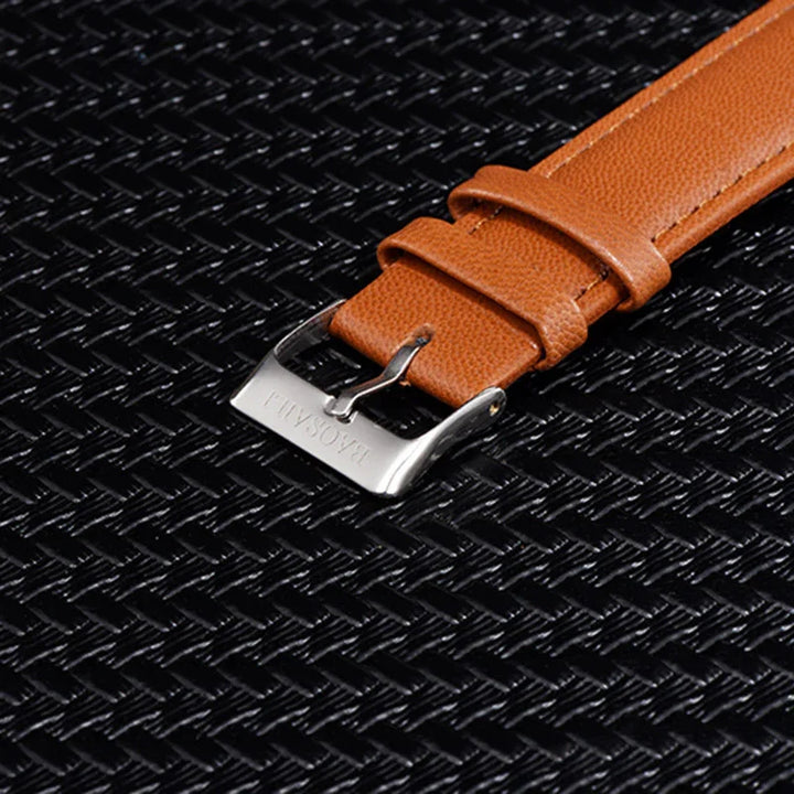 Brown leather watch strap with silver buckle engraved with 'BASICALI' on black textured surface