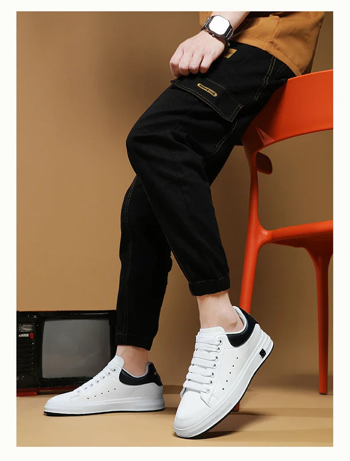 Person wearing white and black sneakers with black cargo pants sitting on orange chair against brown background