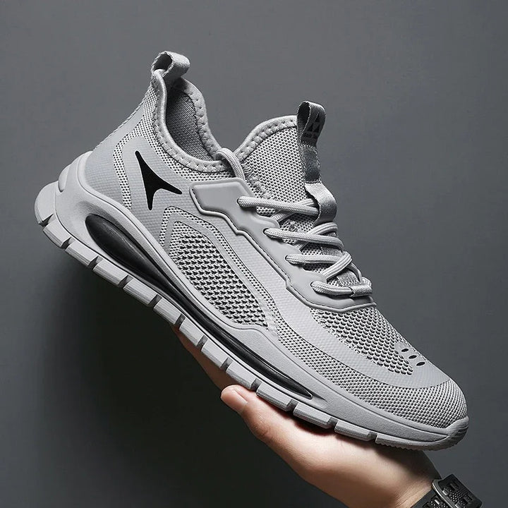 Gray breathable mesh athletic sneaker with black accents and cushioned sole held against gray background