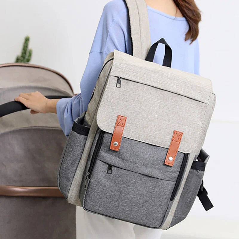 Two-tone beige and gray backpack with brown straps worn by person pushing baby stroller