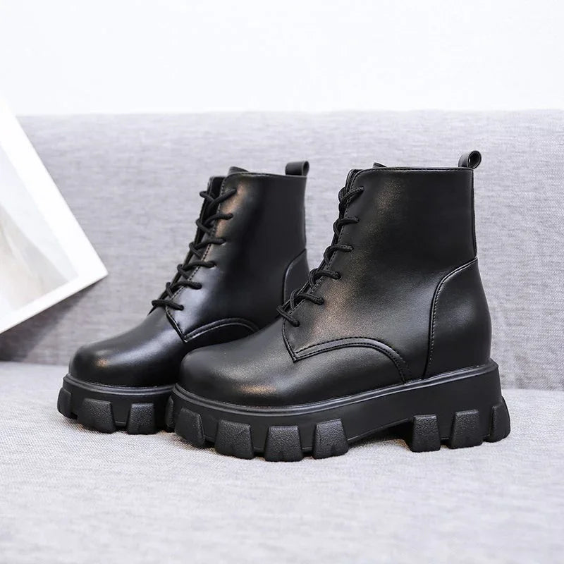 Black leather combat boots with chunky treaded soles on grey fabric surface