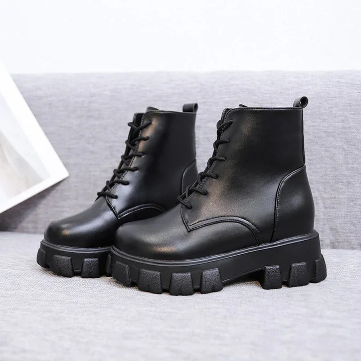 Black leather combat boots with chunky treaded soles on grey fabric surface