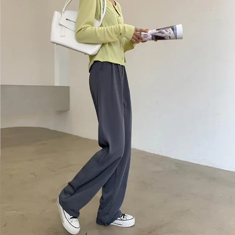 Person wearing loose dark gray pants, light green cardigan, white sneakers, and carrying white shoulder bag indoors