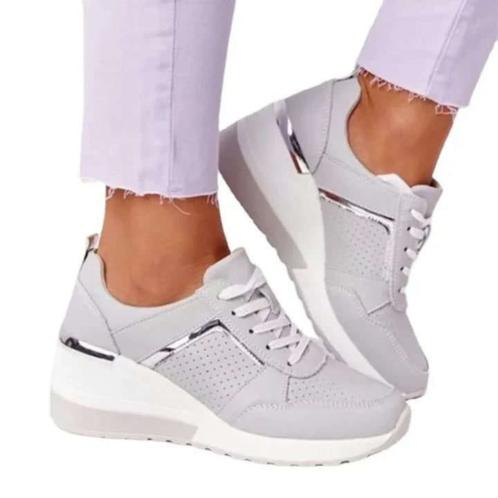 Light gray wedge sneakers with perforated sides and metallic accents worn with light purple frayed jeans