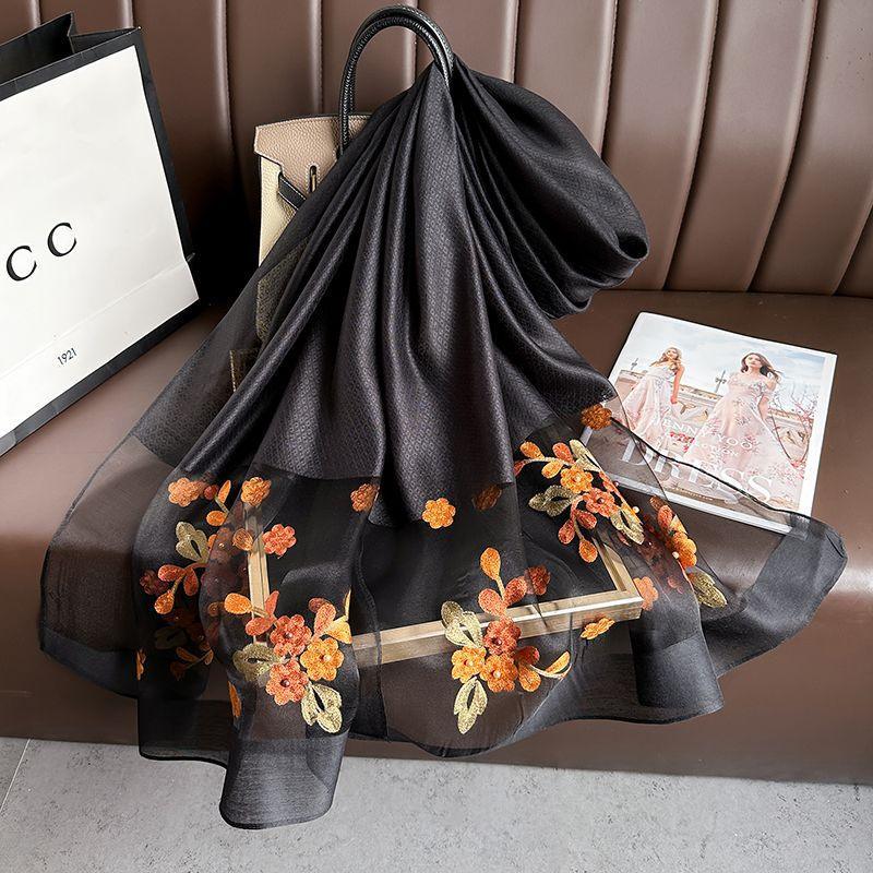 Black sheer scarf with orange floral embroidery draped over brown leather sofa with handbag and fashion magazine