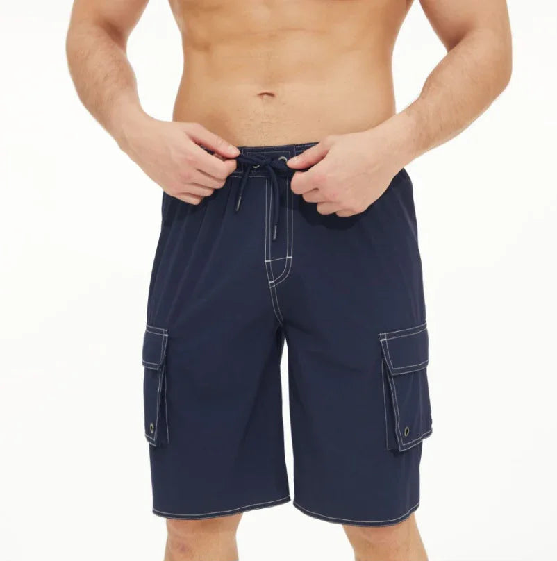 Man wearing navy blue cargo swim shorts with white stitching and drawstring waist on white background