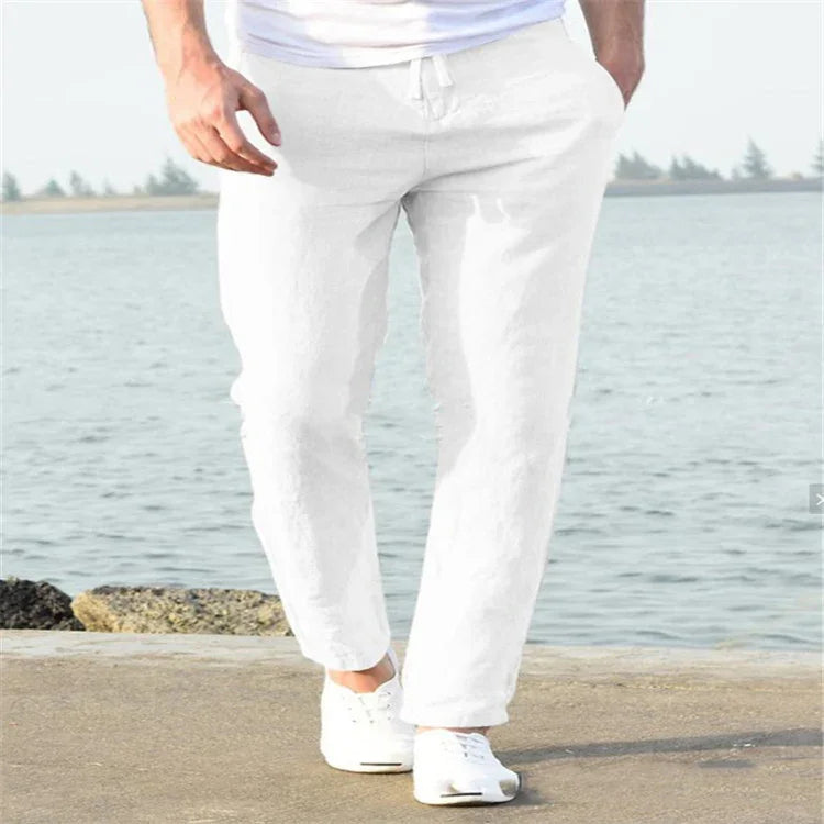 Close-up of man wearing white jogger pants and white sneakers walking by the waterfront on a concrete path
