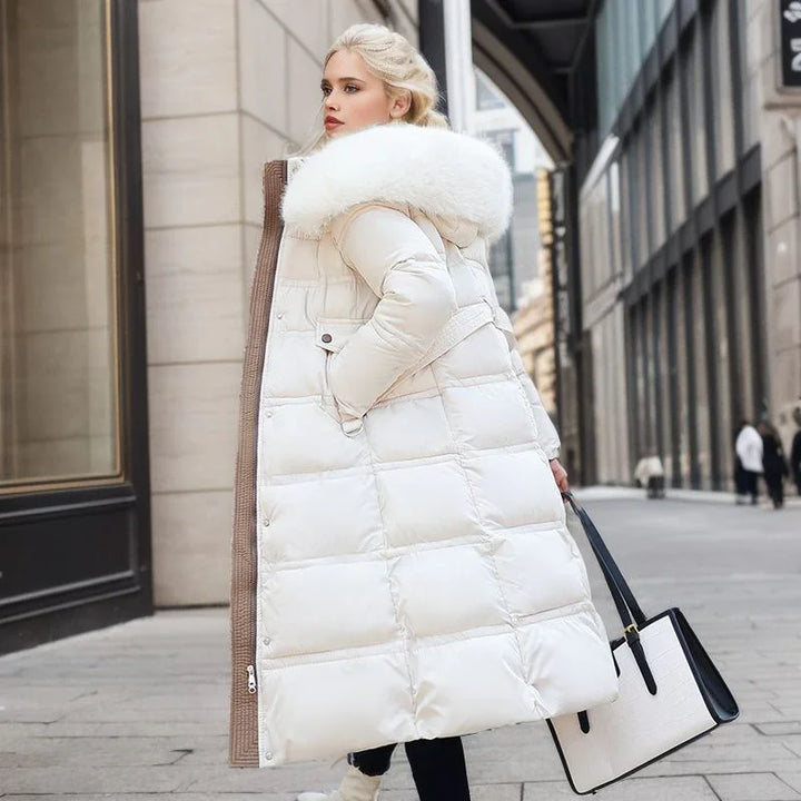 Blonde woman wearing long white puffer coat with fur hood, carrying white and black tote bag in city