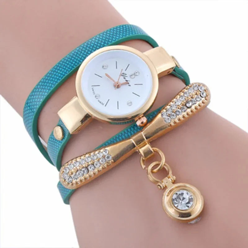 Elegant gold watch with white dial and teal textured wrap strap featuring crystal-studded bow charm