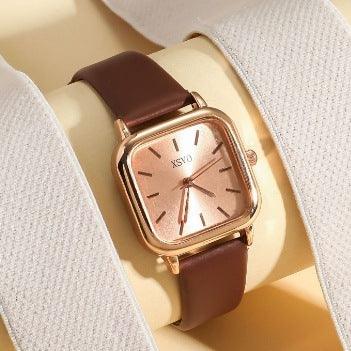 Rose gold square wristwatch with brown leather strap on beige and white fabric background