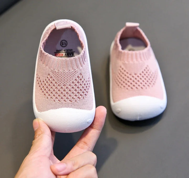 Pink knitted baby shoes with white soles and heart pattern, shown on grey surface