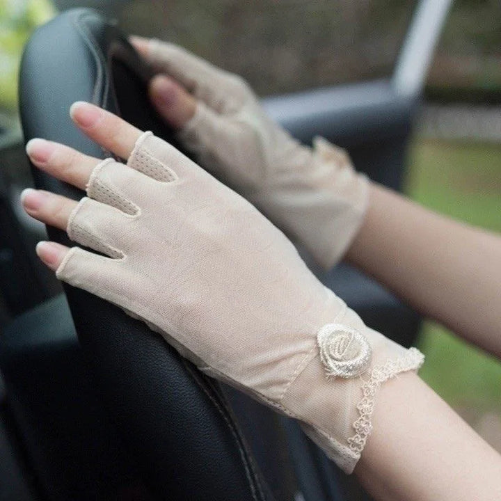 Close-up of hands wearing beige fingerless lace gloves with rose decoration on a black steering wheel