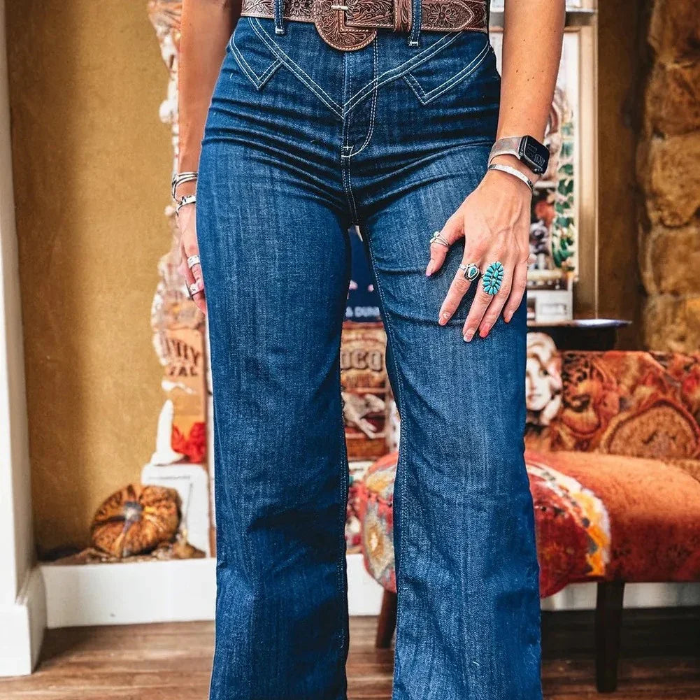 Close-up of person wearing high-waisted flared blue jeans and brown embossed belt with turquoise rings and watch