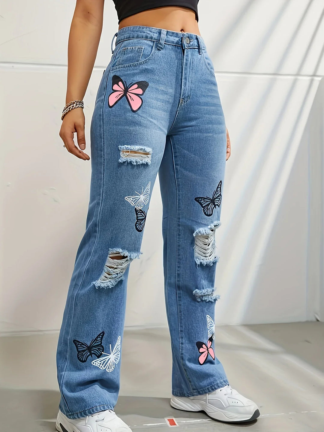 High-waisted blue ripped jeans with pink and black butterfly prints worn with white sneakers