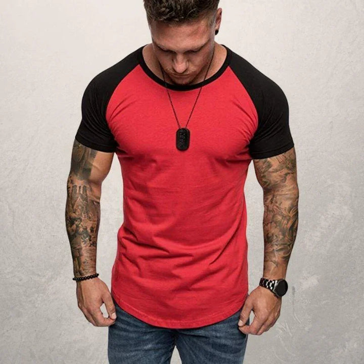 Man wearing a red and black raglan sleeve t-shirt, showing tattooed arms and a black pendant necklace