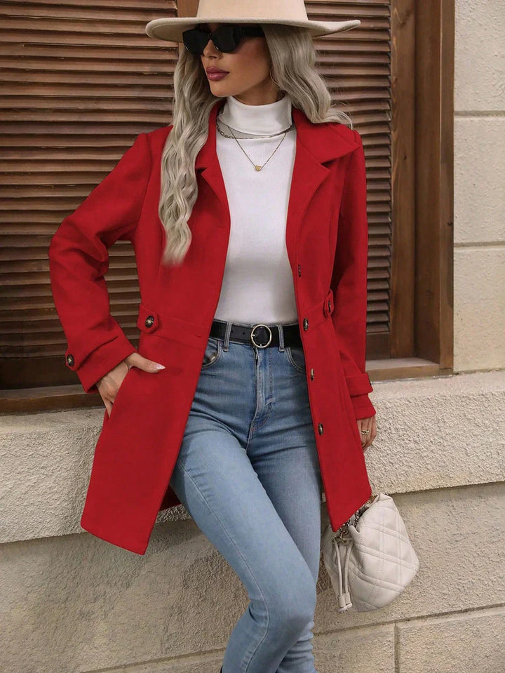Woman wearing red coat with white turtleneck, light blue jeans, beige hat, and sunglasses, holding white quilted handbag
