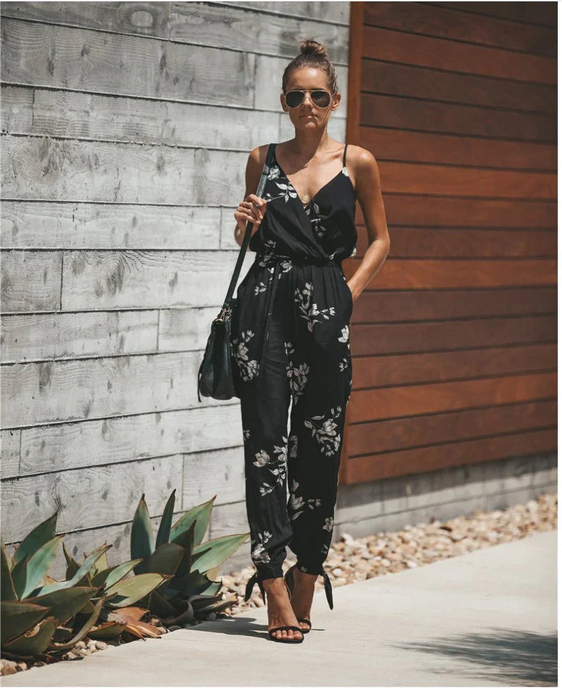 Woman wearing black floral jumpsuit and sunglasses walking on sidewalk with modern wood and concrete wall background