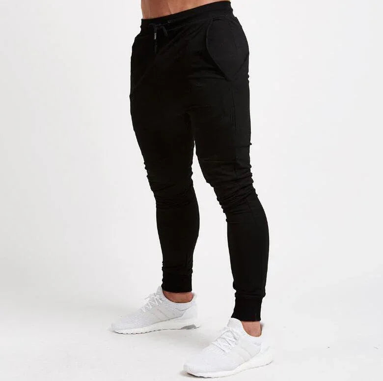 Man wearing black slim-fit jogger pants with pockets and white athletic sneakers on white background