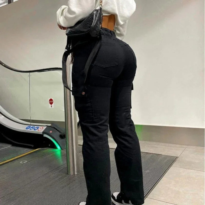 Woman in black cargo pants and white top standing near escalator indoors with black handbag