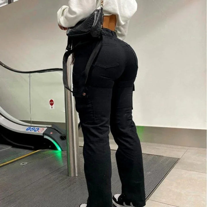 Woman in black cargo pants and white top standing near escalator indoors with black handbag