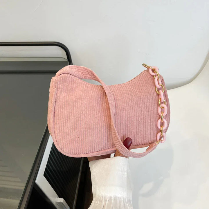 Hand holding a pink corduroy shoulder bag with a pink and gold chain strap on white and black background