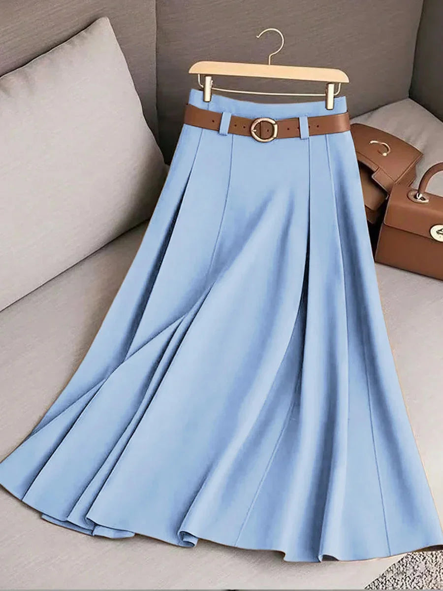 Light blue pleated midi skirt with brown belt hanging on wooden hanger on beige sofa with brown handbags