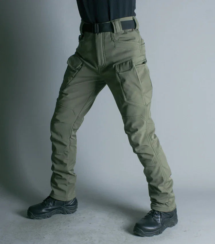 Person wearing olive green tactical pants with multiple pockets and black boots, standing against a plain background