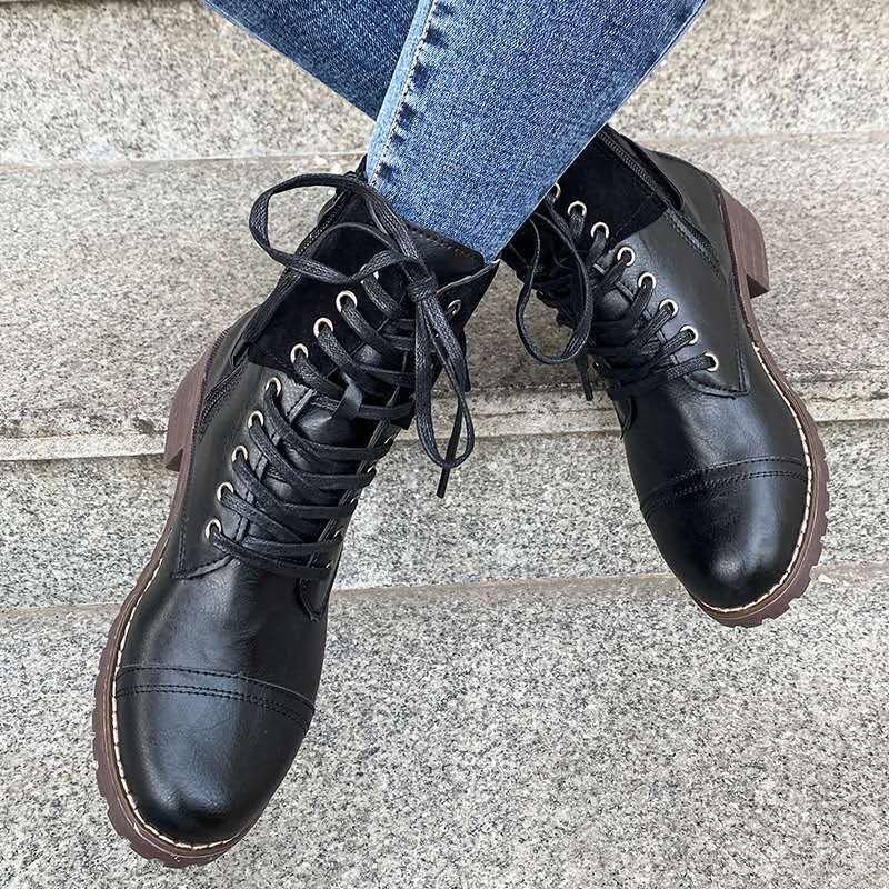 Black leather lace-up ankle boots with brown soles worn with blue denim jeans on stone steps