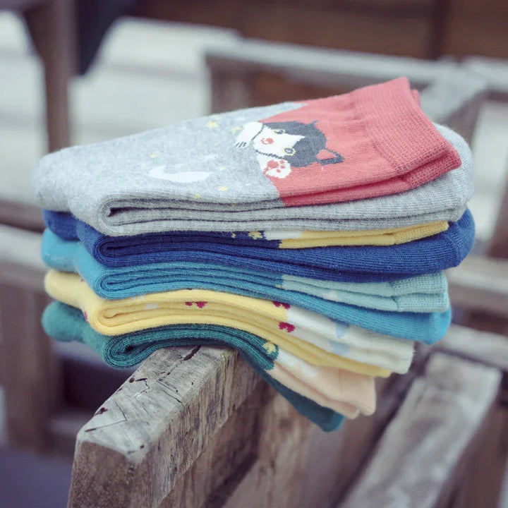 Stack of colorful folded socks with animal and star patterns on rustic wooden bench
