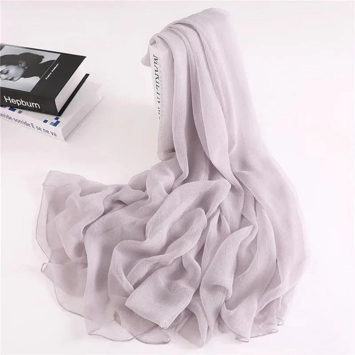 Light purple sheer chiffon scarf draped over white book with soft folds on white background