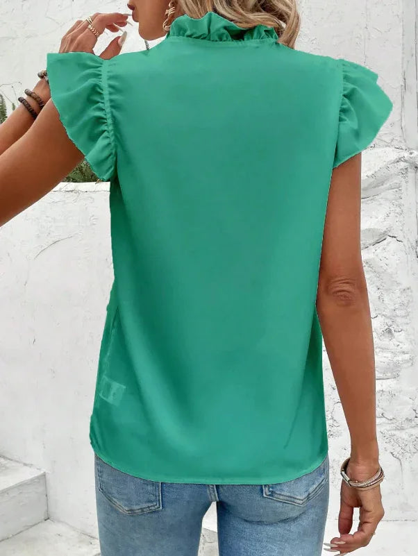 Woman wearing green ruffle sleeve blouse with high collar and blue jeans, back view