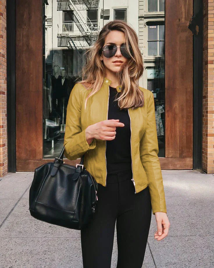 Woman wearing mustard yellow leather jacket, black pants, aviator sunglasses, carrying black leather handbag in urban setting