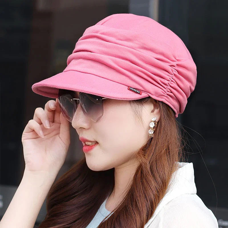 Woman wearing stylish pink ruched cap with tinted sunglasses and pearl drop earrings