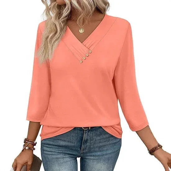 Woman wearing coral pink V-neck 3/4 sleeve casual top with button detail, paired with blue jeans