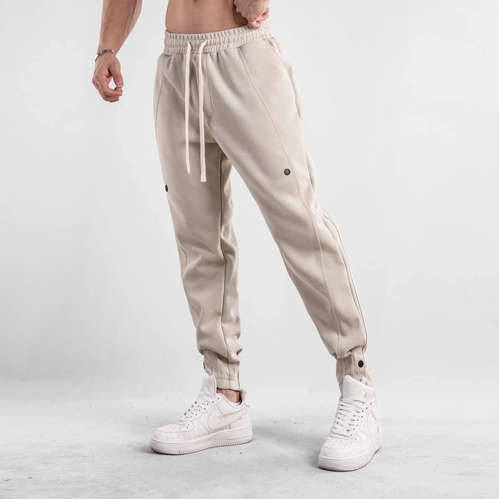 Man wearing beige jogger pants with drawstring and white high-top sneakers against grey background