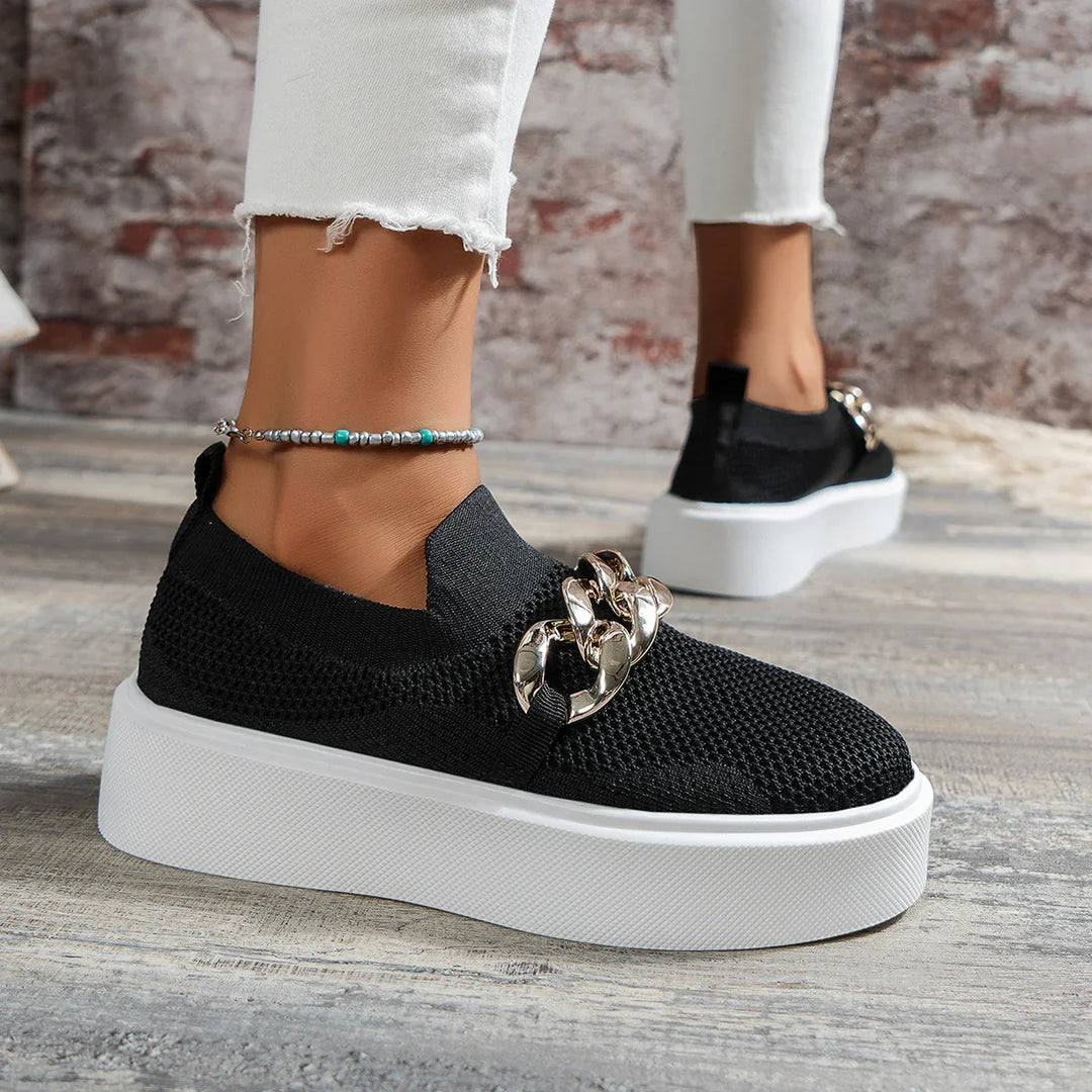 Black knit platform slip-on sneakers with large silver chain detail worn with white frayed hem jeans and a beaded anklet