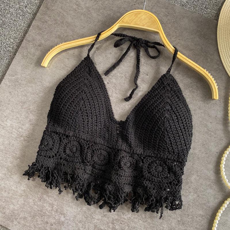 Black crocheted halter crop top with floral pattern and fringed hem on wooden hanger