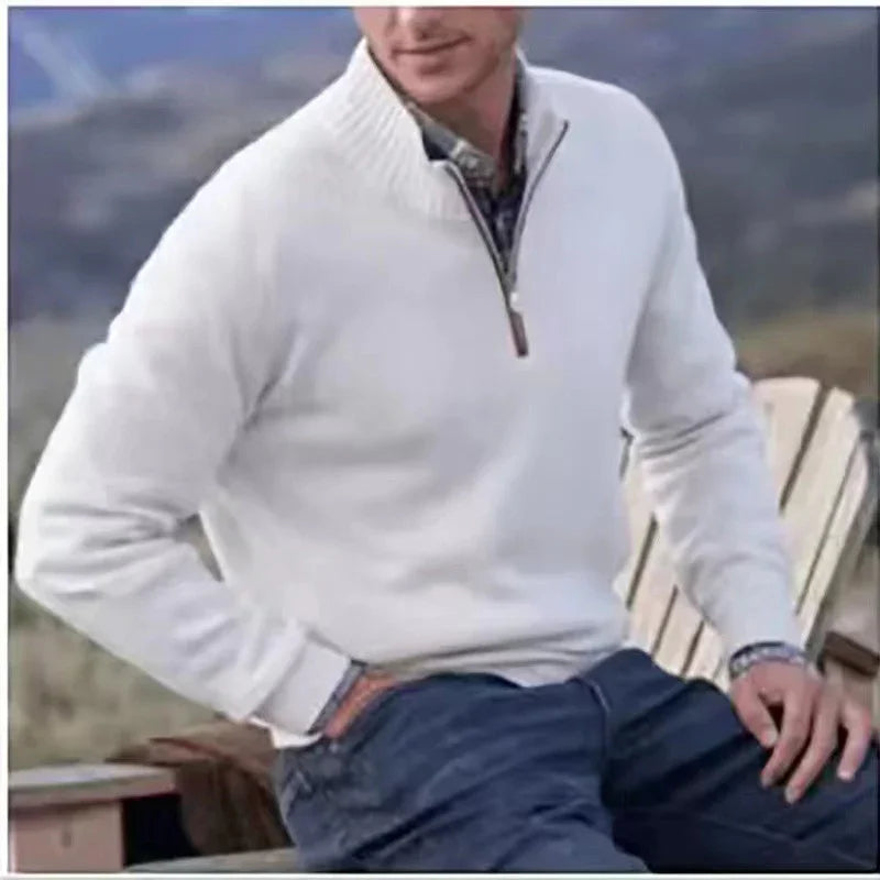 Man wearing white quarter-zip sweater and blue pants sitting outdoors on wooden chair