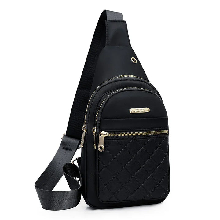 Black quilted sling bag with gold zippers and adjustable strap on white background