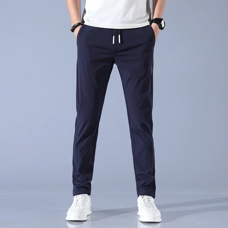 Man wearing navy blue casual jogger pants with white drawstring and white sneakers on gray background