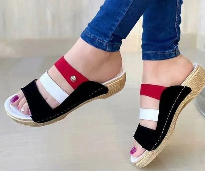Close-up of feet wearing stylish open-toe wedge sandals with red, white, and black straps and denim jeans