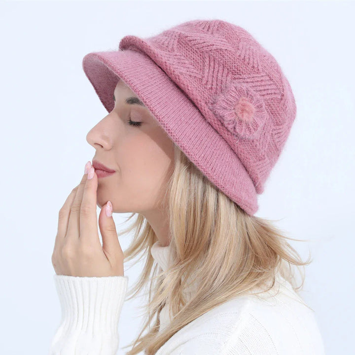 Woman wearing a pink knitted bucket hat with flower detail and a white sweater