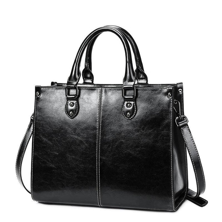 Black leather handbag with double handles and detachable shoulder strap on white background