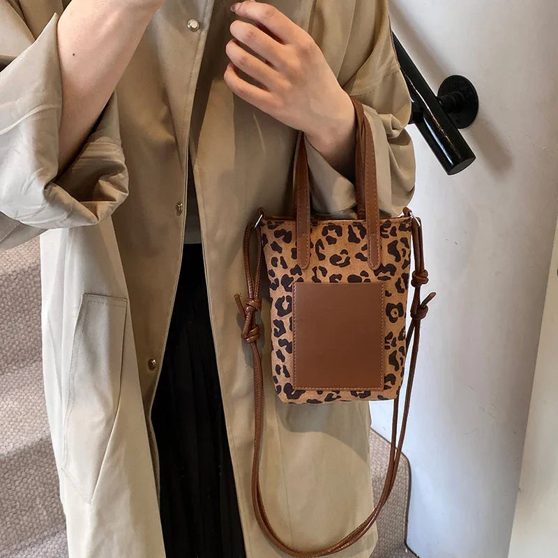Person wearing beige coat holding small leopard print handbag with brown leather front pocket and handles
