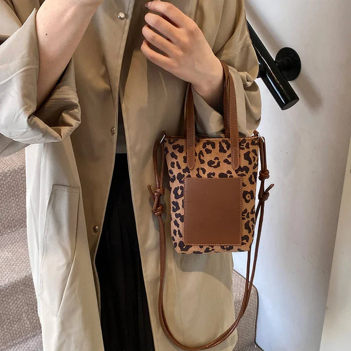 Person wearing beige coat holding small leopard print handbag with brown leather front pocket and handles